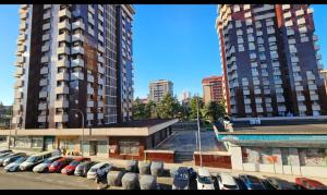 a parking lot with cars parked in front of two tall buildings at piso 3h,5pers,s-c,1b,cocina in Gijón