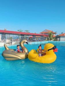 two children are riding on two rubber ducks in a pool at Ruby Star Quỳnh Resort 