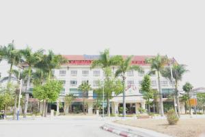 un grand bâtiment blanc avec des palmiers devant lui dans l'établissement Coecco Xieng Khouang Hotel, à Ban Nafèng