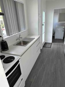 a white kitchen with a sink and a stove at Cozy 3BR West Auckland in Auckland