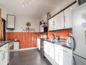 a kitchen with white cabinets and an orange tiled wall at Driftwood Kilgetty in Begelly