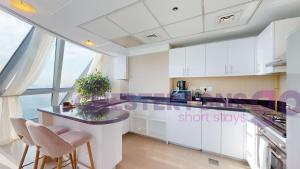 a kitchen with white cabinets and a counter with stools at Chestertons Go - Park Towers - DIFC in Dubai
