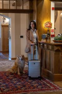 una donna in piedi accanto a un cane con una valigia di Belvedere Dolomites Flower Hotel a Moena