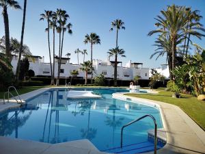 une grande piscine avec des palmiers en arrière-plan dans l'établissement Casa con encanto a 100m de la playa en Marbella, à Marbella