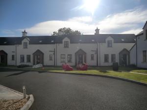 une grande maison blanche avec des chaises rouges dans l'allée. dans l'établissement Ulster Cottages, à Bushmills