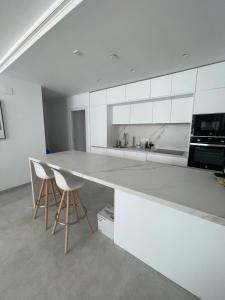 una cocina con un gran mostrador blanco y 2 taburetes en Costa Ballena - Dos dormitorios, Piscina y Jardín privado en Cádiz