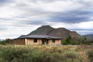 uma casa num campo com uma montanha ao fundo em Samara Karoo Reserve em Graaff-Reinet