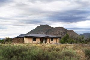 a house in a field with a mountain in the background at Samara Karoo Reserve in Graaff-Reinet