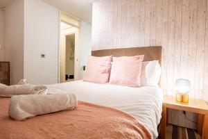 um quarto com uma cama com lençóis brancos e almofadas cor-de-rosa em Cosy Canterbury Studio Apartment em Kent