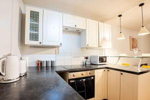 uma cozinha com armários brancos e um balcão preto em Cosy Canterbury Studio Apartment em Kent
