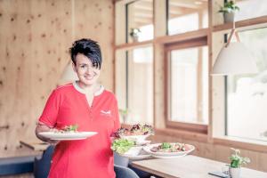 a woman is holding two plates of food at Boutique Hotel LechZeit in Elmen