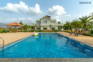 a swimming pool in front of a house at Ekostay Gold Palm Estate I Cricket Turf I Rain Dance I 2 Acre Property in Karjat