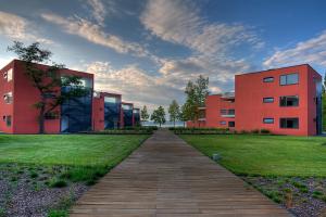 a wooden walkway leading to two red buildings at BL Apartman by HelloBalatonlelle in Balatonlelle