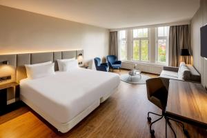 a bedroom with a large white bed and a living room at NH Amsterdam Schiller in Amsterdam