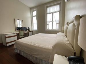 a bedroom with a bed and a desk and two windows at Pousada Magister in Petrópolis