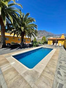 een zwembad met palmbomen en een geel gebouw bij Apartamentos Casa Rosán, junto a la Caldera de Taburiente in El Paso