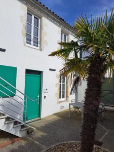 a palm tree in front of a white building with a green door at Les logis de Simon in La Flotte