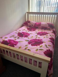 a bed with a pink floral comforter on it at Self contained room, en-suite with separate lockable front door, located in an exclusive area in Wednesbury