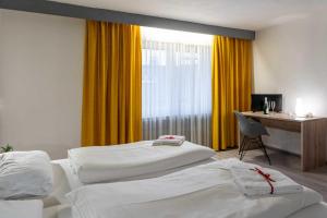 two beds in a room with a desk and a window at Hotel Wildpferd Dülmen in Dülmen