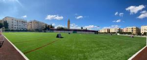 um grande campo verde com edifícios ao fundo em Eventi Club by cité des sports adarissa em Fez