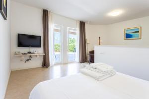 een witte slaapkamer met een bed en een televisie bij Apartments Keti in Splitska