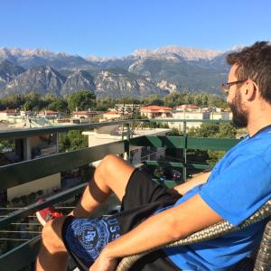 um homem sentado numa varanda com vista para as montanhas em Hellas Palace ROOMS LOFT em Sparti