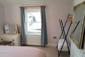 1 dormitorio con cama, espejo y ventana en Quaint 3 bedroom Devon cottage en Honiton