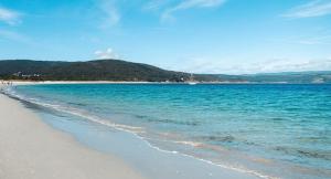 a beach with blue water and a boat in the distance at Piso da Charca in Fisterra