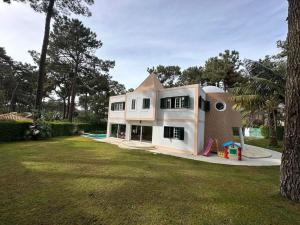 ein großes weißes Haus mit einem Spielplatz im Hof in der Unterkunft Golf, Pool and Beach Aroeira Villa in Aroeira