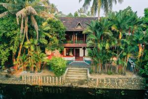 a house with palm trees next to the water at Garggi Backwater Retreat in Kottayam