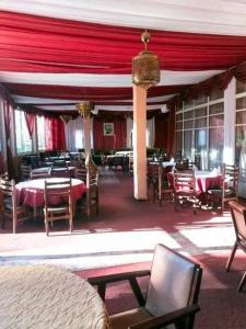 un comedor con mesas, sillas y cortinas rojas en Hôtel El Ayachi en Midelt