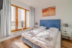 łóżko z niebieskim zagłówkiem w pokoju z oknami w obiekcie 3L Apartments Olympic Park w Kołobrzegu