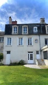 a large white house with white doors and a grass yard at Le Hêtre Pourpre in Bayeux