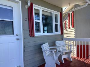 - une terrasse couverte avec 2 chaises blanches et une table dans l'établissement Hôtel-Motel Rocher Percé, à Percé