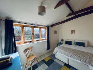 a bedroom with a bed and a chair and windows at Little Owl Cottage in Saxmundham