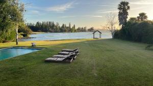 a group of benches sitting on the grass next to a pool at Preciosa Casa con Piscina y muelle en orilla Lago Rapel in Las Cabras