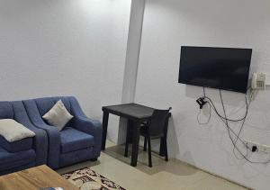 a living room with a blue chair and a table with a tv at نور المنازل للوحدات السكنية in Qarār