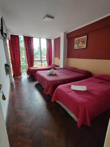 3 łóżka w pokoju z czerwonymi ścianami i oknami w obiekcie Hotel Ery Noa w mieście San Salvador de Jujuy