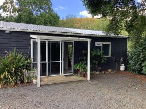 un petit hangar noir avec une porte ouverte dans l'établissement Wood Pigeon Cottage Pet Friendly Free Breakfast Hauraki Rail Trail 2kms, à Waikino