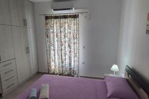 1 dormitorio con cama morada y ventana en Larinaki's Cozy Apartment No1, en Órmos Aiyialís