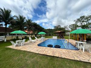 una piscina con sillas y sombrillas verdes en Pousada Geres Peruíbe, en Peruíbe