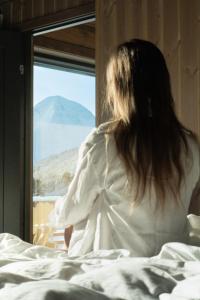 una mujer sentada en la cama mirando por una ventana en Unique Romantic Cabin with Mountain View at Strandafjellet, Mivo X, en Stranda