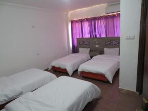 three beds in a room with pink curtains at Best hotel aqaba in Aqaba