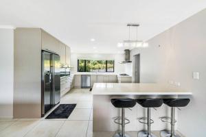 a kitchen with a large white counter and stools at Luxury Modern 3-BDR Oasis in Kumeu