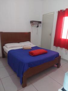 a bed with a blue blanket and a red pillow on it at Jardim Paraíso in Duque de Caxias