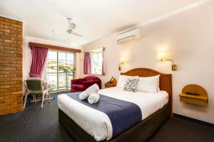 Habitación de hotel con cama y silla en Sapphire Waters Motor Inn en Merimbula