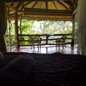 a bed in a room with two chairs and a porch at On The Rocks Bungalows, Restaurant and Jungle Trekking Tours in Bukit Lawang