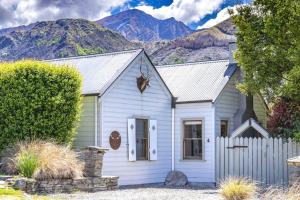 a small white house with mountains in the background at Stags Head Cottage-cosy cottage with hot tub in Arrowtown