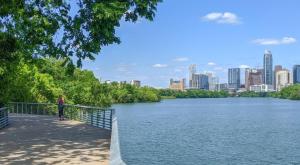 a person standing on a sidewalk next to a river with a city at Château at Lake Austin - 10 Min Walk to Center DT in Austin