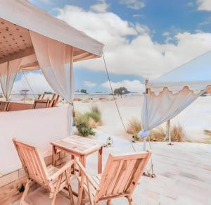 eine Terrasse mit Stühlen, einem Tisch und einem Sonnenschirm in der Unterkunft Griat sandy desert camp jaisalmer in Jaisalmer